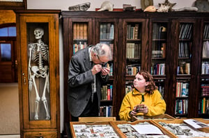 Professor looking at fossils and a student looking up at professor with phone